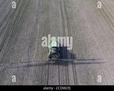 Trattore con sistema incernierato di irrorazione di pesticidi. Concimazione con un trattore, sotto forma di aerosol, sul campo d'inverno Foto Stock