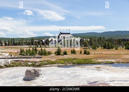 Guardando attraverso il terreno vulcanico e il fiume Firehole fino al Old Faithful Inn con auto e turisti godendo il sole Giornata estiva a Yellowstone Nati Foto Stock