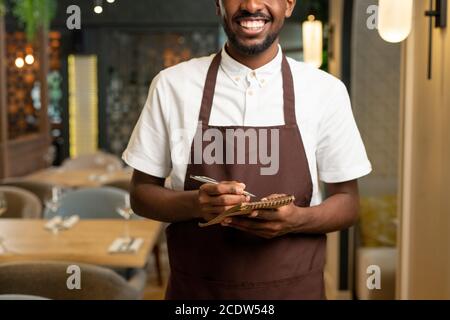 Mani di giovane cameriere con sorriso togoteo tenendo penna e. blocco note piccolo Foto Stock