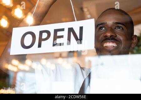Felice giovane lavoratore di caffè appendere carta con avviso aperto sportello trasparente Foto Stock