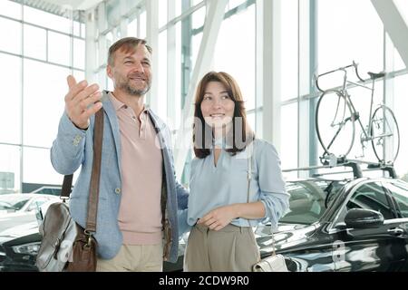 Felice uomo maturo in casualwear intelligente mostrando la sua moglie sorridente varietà di auto Foto Stock
