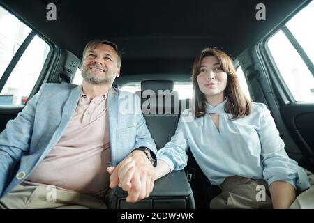 Affettuoso felice marito e moglie di mezza età seduti sul sedile posteriore di auto nuova Foto Stock