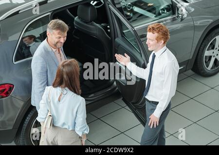 Giovane ed elegante responsabile vendite che mostra ai clienti l'interno di nuovo modello di auto Foto Stock