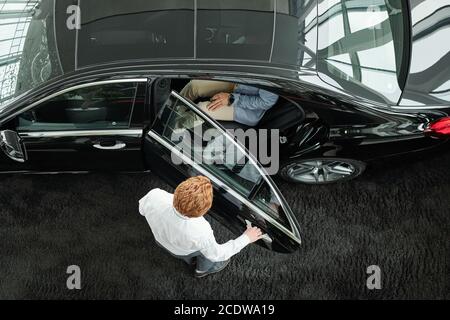 Responsabile vendite che chiude la porta dell'auto con i clienti all'interno prima della prova su strada Foto Stock