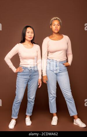 Due giovani eleganti donne di etnie africane e asiatiche abbigliamento casualwear Foto Stock