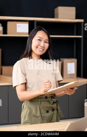 Felice giovane donna asiatica con penne e appunti liste di controllo degli ordini dei clienti Foto Stock
