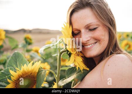 Primo piano di una giovane donna sorridente con gli occhi chiusi a contatto girasole sulla faccia a campo Foto Stock