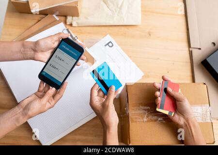 Panoramica delle mani di due manager donne che tengono uno smartphone e. schede di plastica Foto Stock