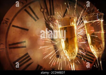Due bicchieri di champagne contro le luci di festa e orologio a mezzanotte Foto Stock