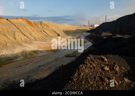 Area abbandonata con acqua sporca in fiume e suolo tossico circondato da colline Foto Stock