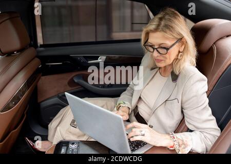 Donna matura in occhiali e grigio Formalwear digitando sul computer portatile tastiera Foto Stock