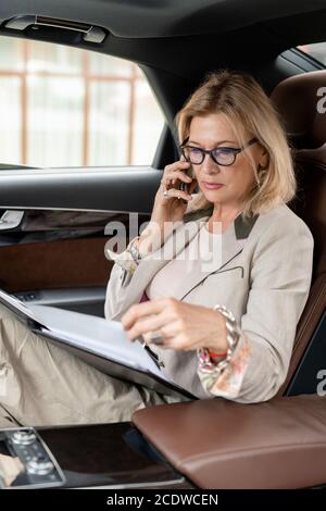 Donna d'affari seria matura seduta sul sedile posteriore del taxi e. telefonando Foto Stock