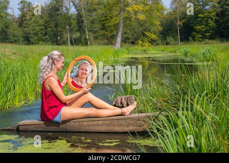 La giovane donna si siede con lo specchio all'acqua nella natura Foto Stock