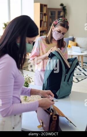 Teenage studentessa contemporanea in maschera protettiva mettendo i libri nello zaino Foto Stock