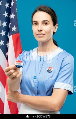 Giovane cameriera contemporanea in uniforme blu che mostra di votare insignia Foto Stock