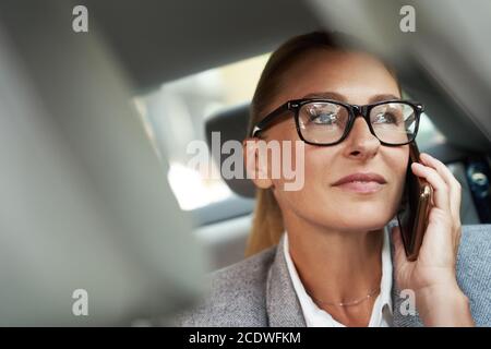 Business talk. Ritratto di una donna d'affari sicura e di successo che indossa occhiali che parlano dal telefono cellulare mentre si siede sul sedile posteriore in auto Foto Stock