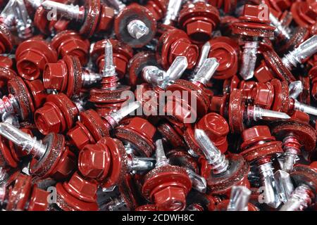 Vista dall'alto della struttura dello sfondo delle viti per tetti. Sfondo rosso viti copertura. А mazzetto di viti autofilettanti per il fissaggio del tetto con teste rosse Foto Stock