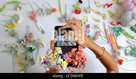 Incredibile vista dall'alto tempo di scatto prodotto a crochet fatto a mano da fotografo femminile, linguetta a due mani, scatta foto da colorate opere d'arte floreali su bianco Foto Stock