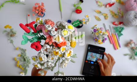 tempo di scatto uncinetto prodotto a mano della fotografa femminile, mazzo di fiori colorati in mano come rosa, margherita, foglia e scattare foto tramite linguetta su bianco Foto Stock