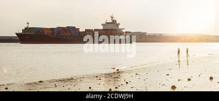 Grande nave container e spiaggia della città sul fiume Elba ad Amburgo, Germania, durante il tramonto panoramico Foto Stock