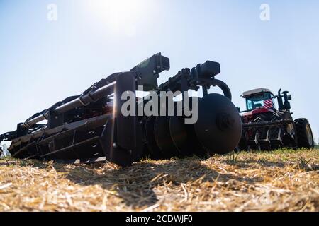 Un trattore con un aratro aratura il campo dopo la mietitura Foto Stock