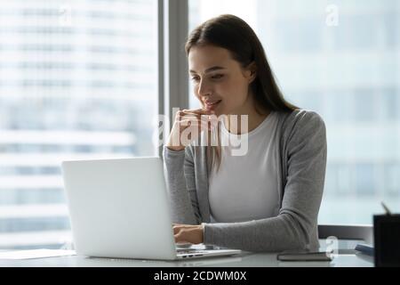 Giovane donna sorridente che usa un computer portatile, seduto alla scrivania in un ufficio moderno Foto Stock