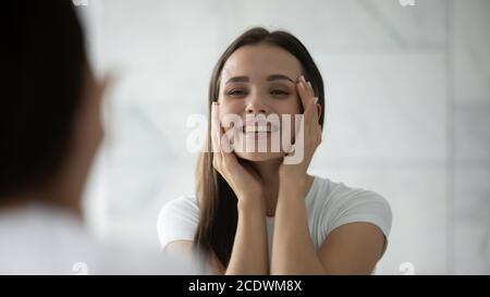 Primo piano testa ha girato sorridendo giovane donna che tocca la pelle del viso Foto Stock