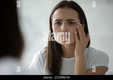 Primo piano testa shot infelice giovane donna che controlla la pelle Foto Stock