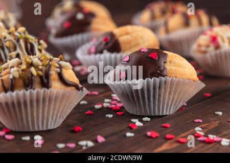 macro foto di biscotti fatti in casa a forma di noci con crema, ciliegina di cioccolato su tavola di legno come sfondo. zucchero rosso, rosa e bianco spolverare i cuori e. Foto Stock