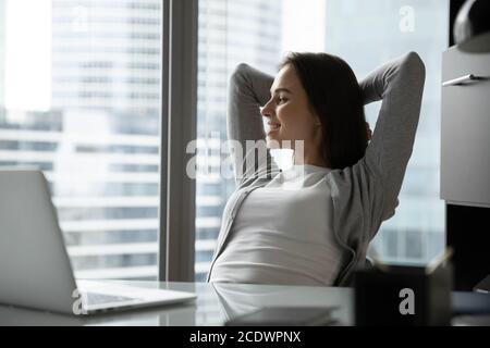 Sognante donna d'affari sorridente che si rilassa in sedia da ufficio, guardando da parte Foto Stock