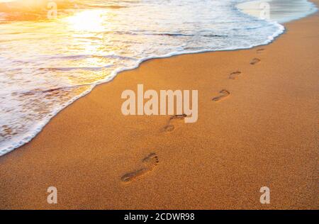 Spiaggia, onde e passi al tramonto Foto Stock