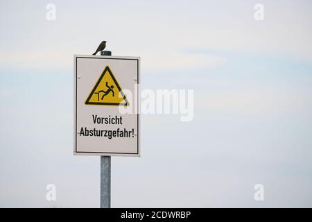 Segno con l'iscrizione attenzione, pericolo di caduta. Sul segno siede un uccello. Foto Stock