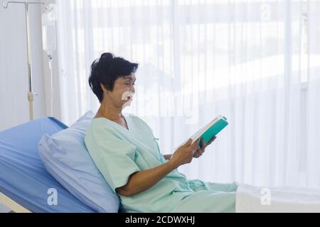 Le donne asiatiche anziane sedettero sul letto per leggere in ospedale. Foto Stock