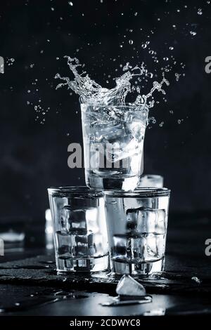 Vodka splash con spray da bicchieri da shot su fondo di pietra nera, bevanda forte ghiacciata in vetro appannato Foto Stock