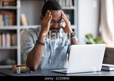 Stressato uomo d'affari afro-americano che tocca templi, che soffrono di mal di testa Foto Stock