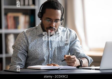 Uomo afro-americano serio messo a fuoco che indossa le note di scrittura delle cuffie Foto Stock