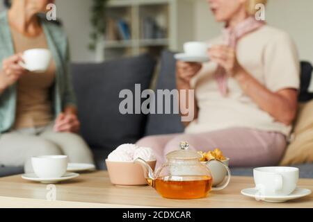 Primo piano della teiera con tè e tazze sul tavolo e due donne che parlano l'una con l'altra sul divano sullo sfondo Foto Stock