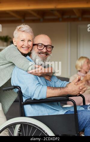 Ritratto della donna anziana felice abbracciando il suo marito disabile e. sorridono alla macchina fotografica Foto Stock