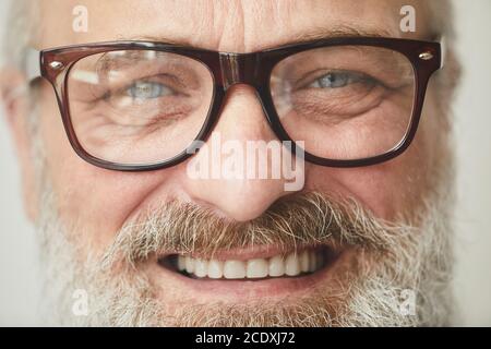 Primo piano di un uomo anziano in occhiali sorridente alla telecamera Foto Stock