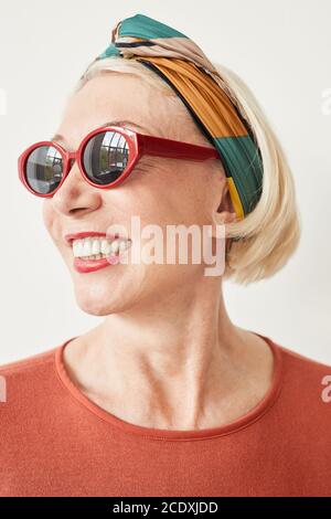 Ritratto di donna matura di moda in eleganti occhiali da sole che sorridono contro lo sfondo bianco Foto Stock