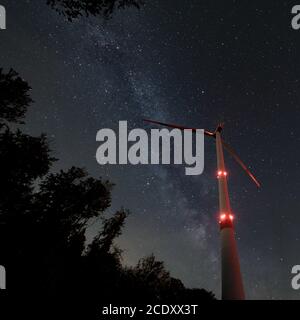 Turbina eolica industriale in mezzo alla foresta, nightshot con strada lattea e cielo stellato. Inversione di tendenza dell'energia di sostenibilità. Foto Stock