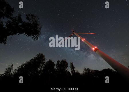 Turbina eolica industriale in mezzo alla foresta, nightshot con strada lattea e cielo stellato. Inversione di tendenza dell'energia di sostenibilità. Foto Stock