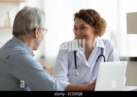 Donna sorridente dottore che ascolta le lamentele di pazienti maturi durante la riunione Foto Stock