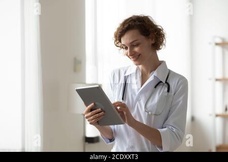 Donna sorridente professionista medico utilizzando tablet digitale, in piedi in ufficio Foto Stock