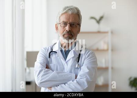 Head shot ritratto medico maturo indossare occhiali in piedi in ufficio Foto Stock