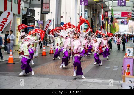 Una squadra giapponese di ballerini yosakoi che indossano yukata a maniche lunghe e sciarpe sventolanti sopra la testa, danzando in galleria per lo shopping, durante Kyusyu Gassai. Foto Stock