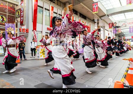 Una squadra giapponese di ballerini yosakoi che indossano yukata a maniche lunghe e che usano naruko, clapper in legno, che ballano in una galleria di negozi, durante Kyusyu Gassai. Foto Stock