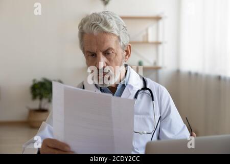 Serio medico maturo che legge il documento medico, lavorando in ufficio Foto Stock