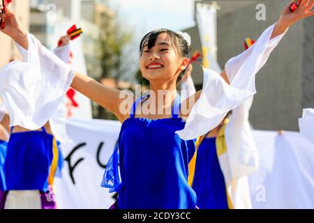 Primo piano giovane ballerina giapponese yosakoi con naruko, clapper in legno, che balla con altri ballerini dietro di lei al festival Kyusyu Gassai. Foto Stock