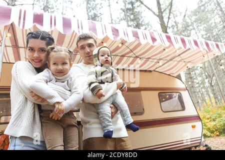 Ritratto di una giovane famiglia sorridente mentre abbracciava vicino a casa sulle ruote Foto Stock